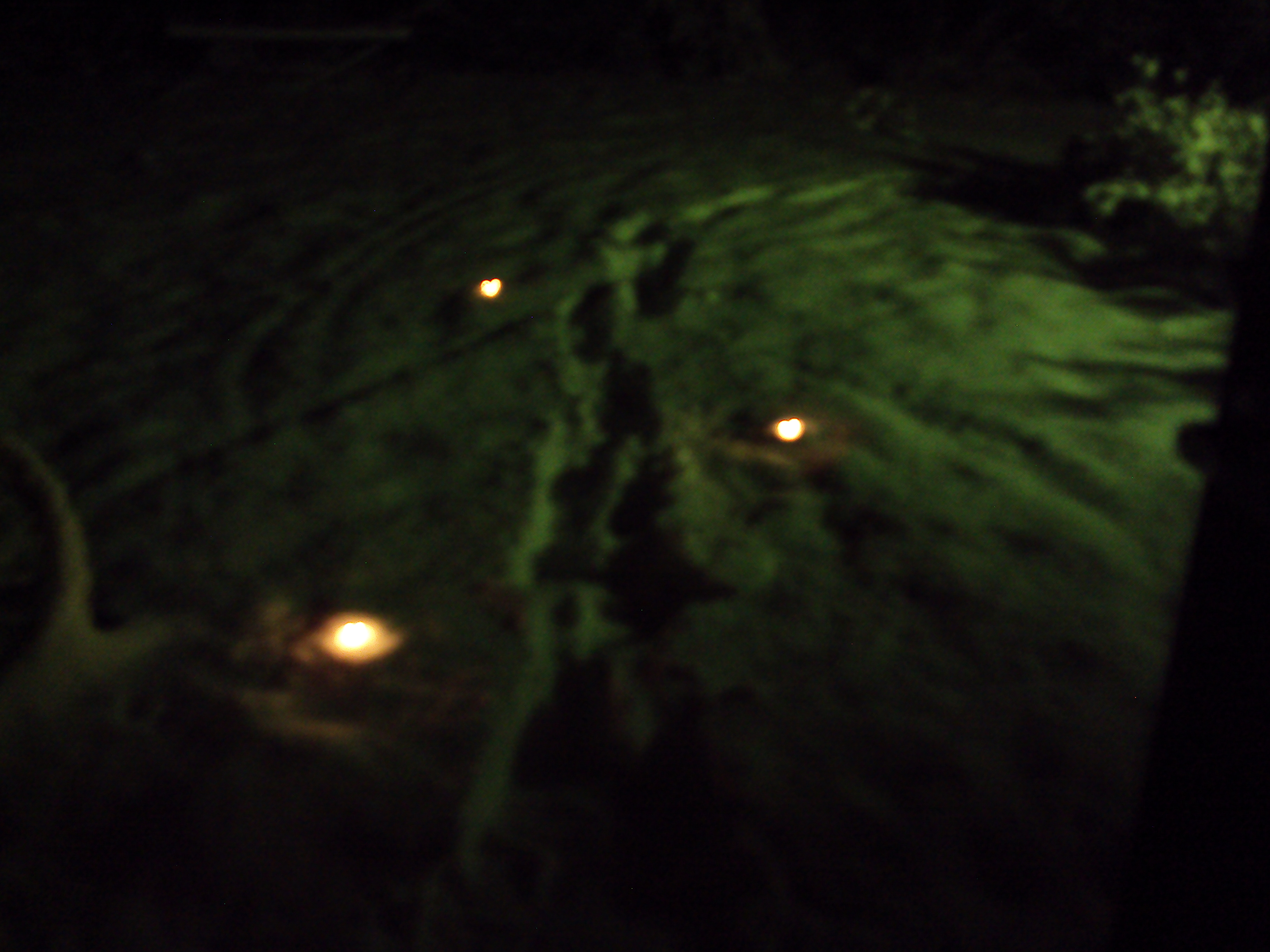 Three teacandles set along a path of footprints in the snow.